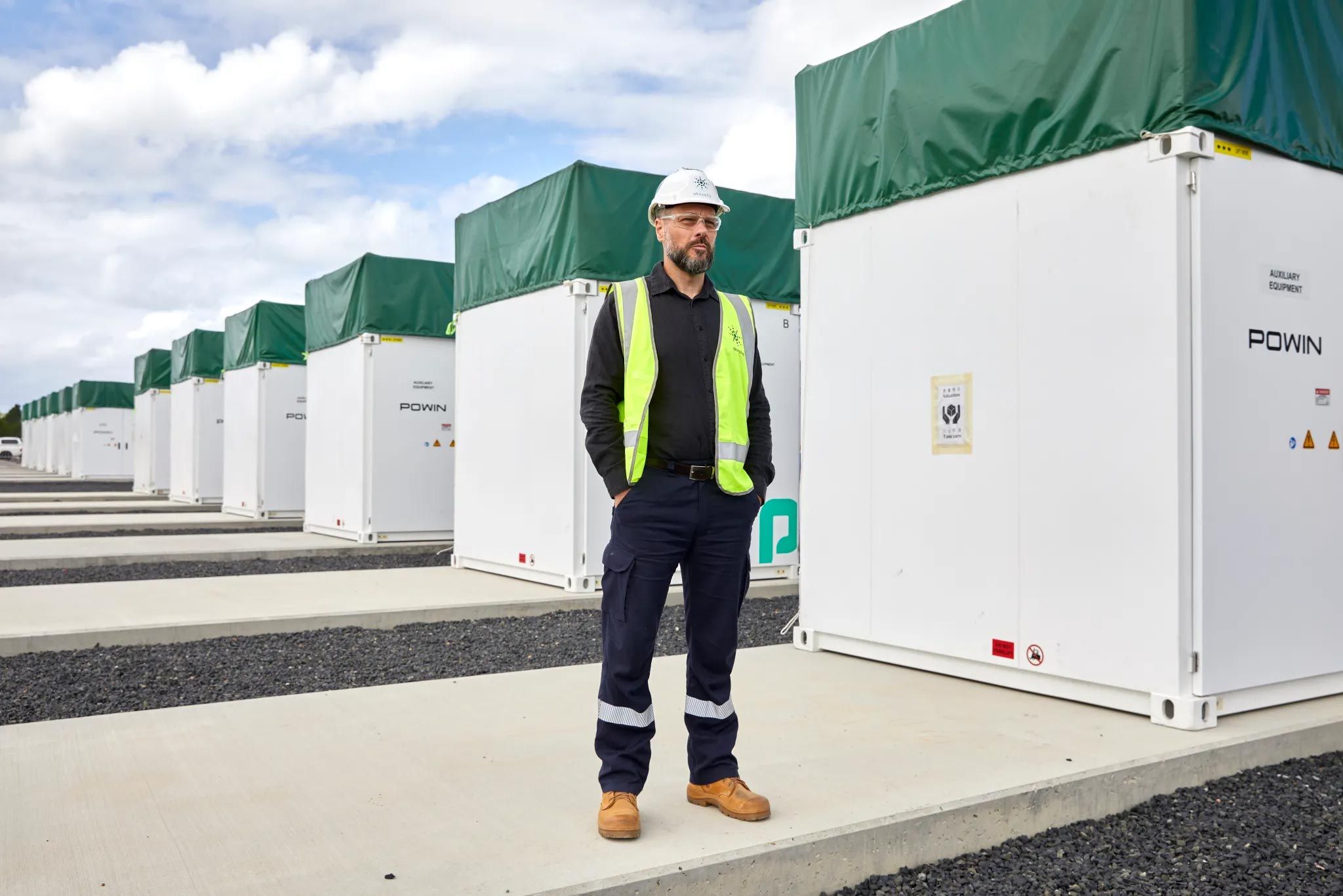 Akayahsa CEO Nick Carter wearing a hard hat and high vis vest standing in front of a row of batteries under construction at the Waratah Super Battery site