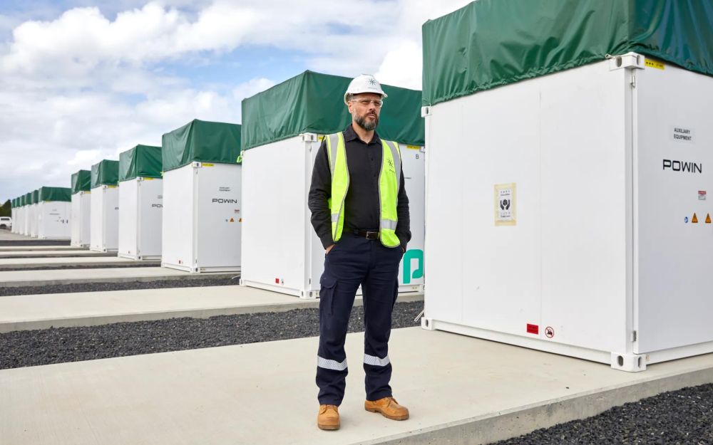 Akayahsa CEO Nick Carter wearing a hard hat and high vis vest standing in front of a row of batteries under construction at the Waratah Super Battery site